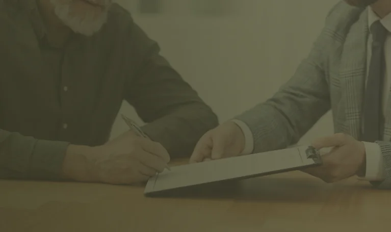 Two men seated at a table, focused on signing documents, with pens in hand and paperwork spread out before them.