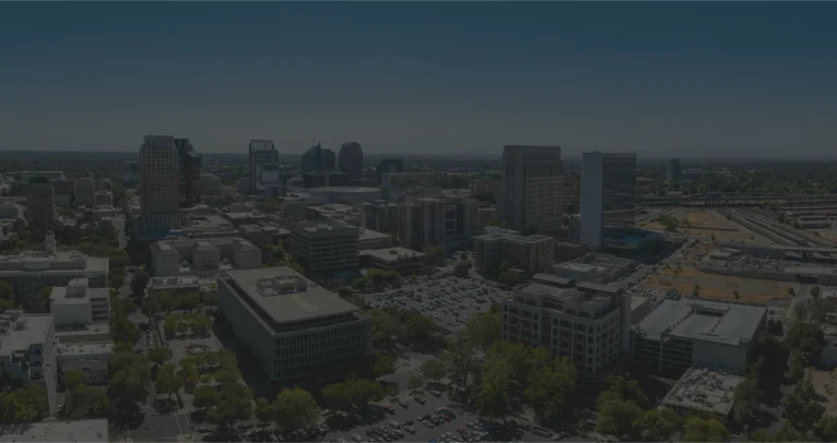Aerial view of the city showcasing buildings, streets, and green spaces under a clear blue sky.