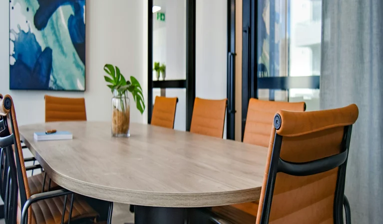 A conference table surrounded by orange chairs, with a colorful painting hanging on the wall behind it.