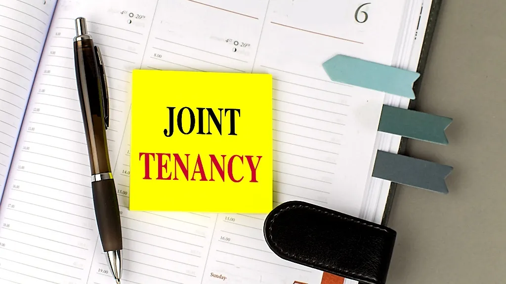 Open planner with blue page markers, black pen, and yellow sticky note reading "JOINT TENANCY