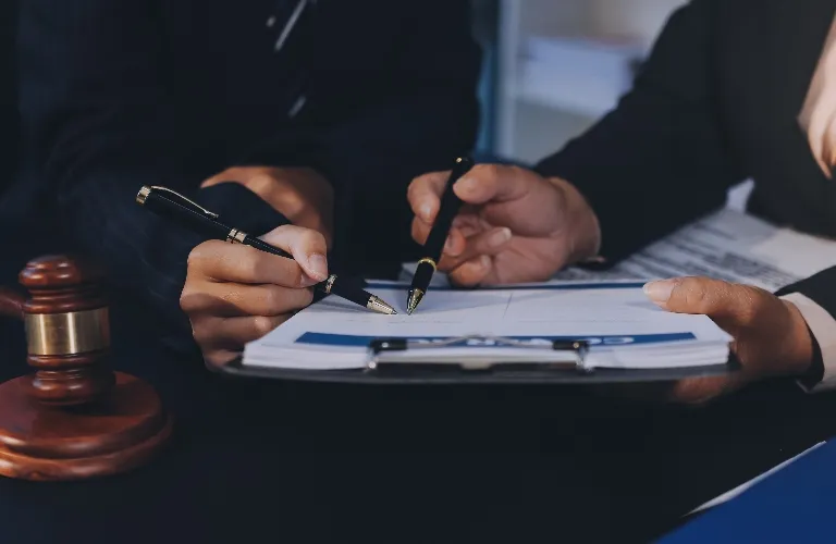 Two individuals in formal attire reviewing and signing documents on a clipboard, with a wooden gavel nearby.