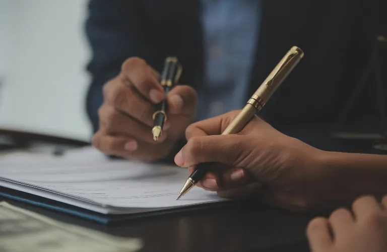 Close-up of two people holding pens and reviewing documents on a table.